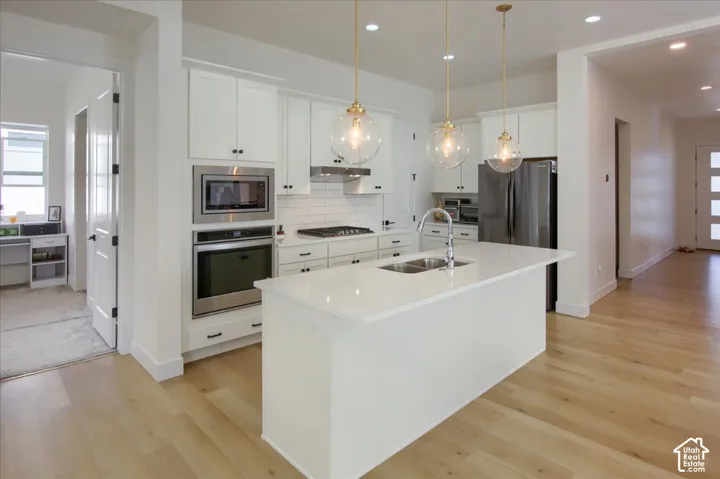 Kitchen featuring a center island with double basin sink, stainless steel appliances, white cabinetry, and wood-finish flooring
