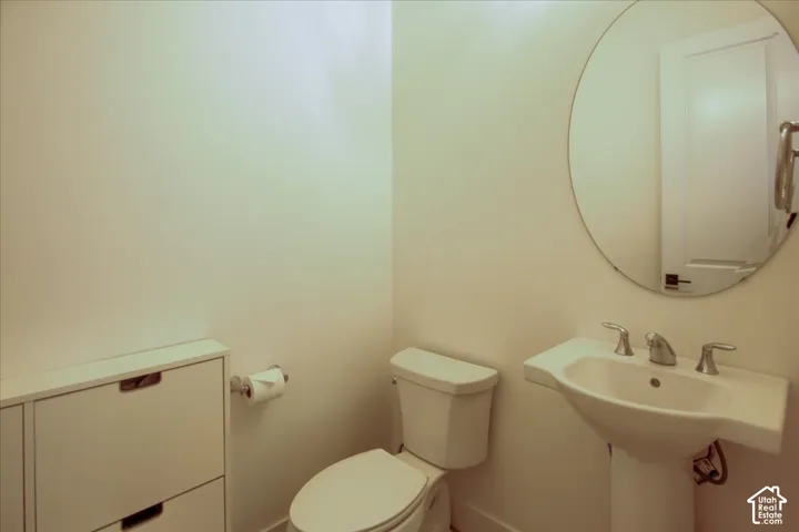 Pedestal sink with chrome fixtures, rounded mirror, and white storage cabinetry