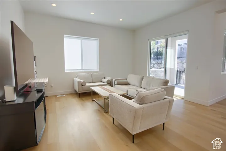 Recessed lighting, wood-finish flooring, sliding glass door, and a large window with roller shades