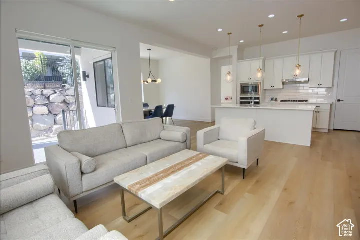 Open-concept living area featuring light wood-finish flooring, white kitchen cabinetry, a kitchen island with seating, a white subway tile backsplash, and a sliding glass door