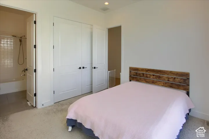 Plush carpet flooring, white interior doors with black hardware, recessed lighting, and an attached bathroom featuring a tile-surround tub/shower combination