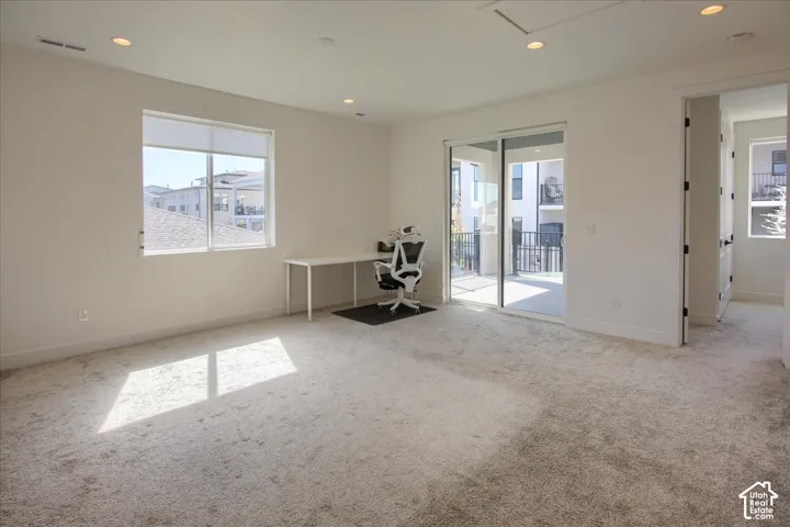 Spacious room featuring neutral carpeting, recessed lighting, a large window, and a sliding glass door leading to an outdoor balcony with black railings