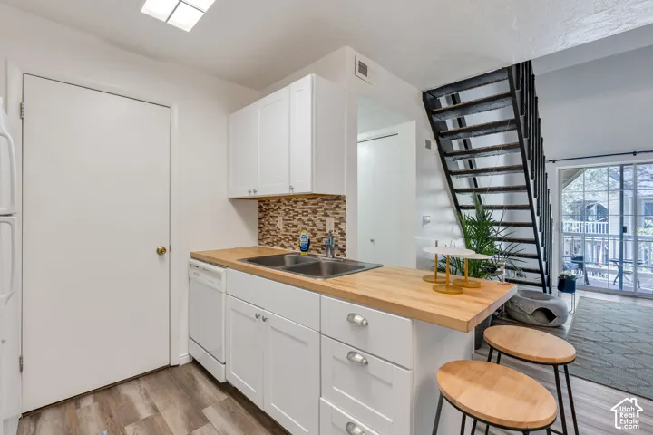 Kitchen featuring white cabinetry, wood-finish countertops, stainless steel double sink, and a mosaic tile backsplash