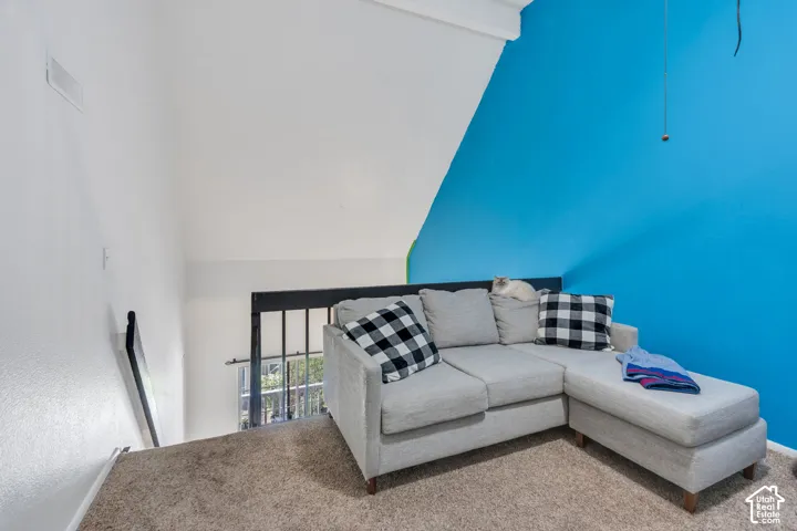 Carpeted loft area with a partial vaulted ceiling and a painted accent wall