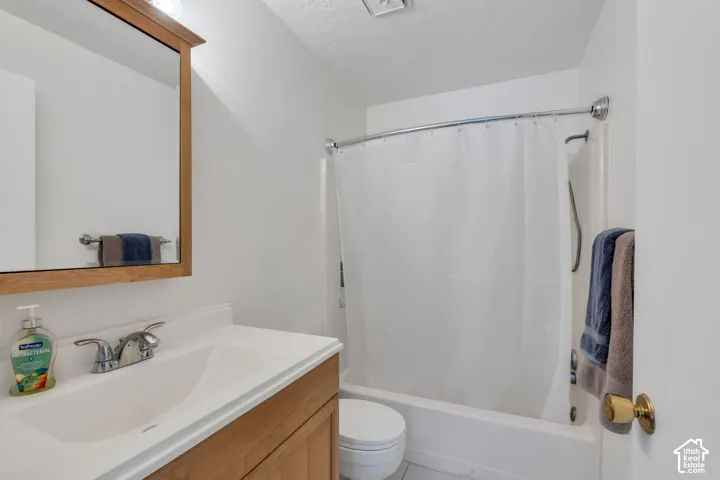 White full-size bathtub with shower, wood-finish vanity with integrated sink, and chrome fixtures