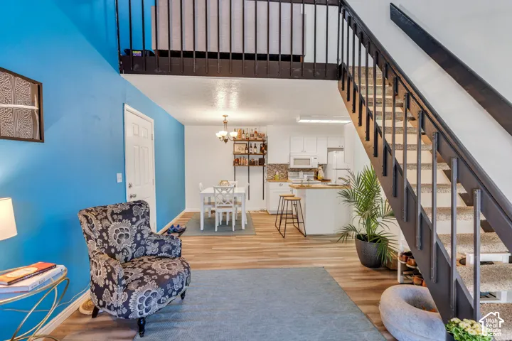 Open-concept living space with wood-finish flooring, a kitchen featuring white cabinetry, and a dining area with a chandelier