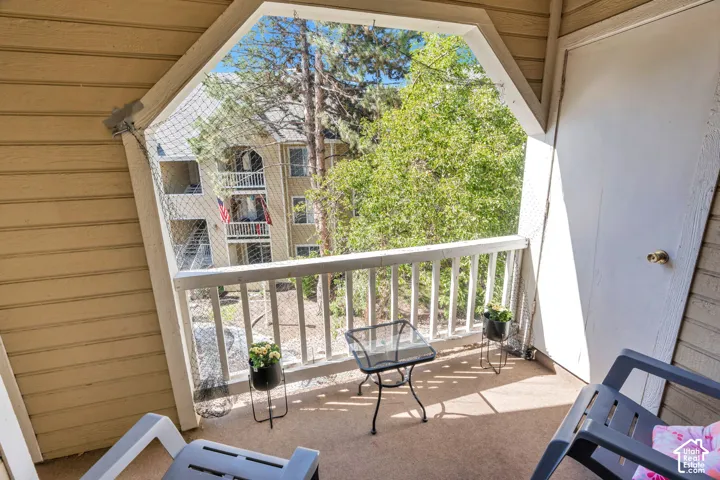 Outdoor balcony with a protective mesh enclosure, white wood-finish railing, and a textured floor surface
