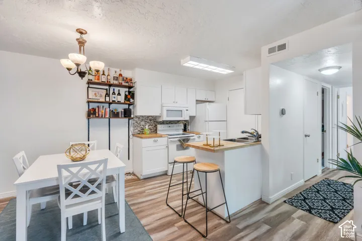 White cabinetry, tile backsplash, wood-finish flooring, built-in shelving, and a bar seating area
