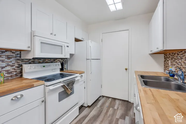 White cabinetry, wood-finish countertops, mosaic tile backsplash, stainless steel double-basin sink, and wood-finish flooring