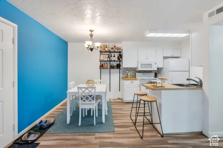 Wood-finish flooring throughout, white kitchen cabinetry, stainless steel sink, tile backsplash, and overhead lighting fixture
