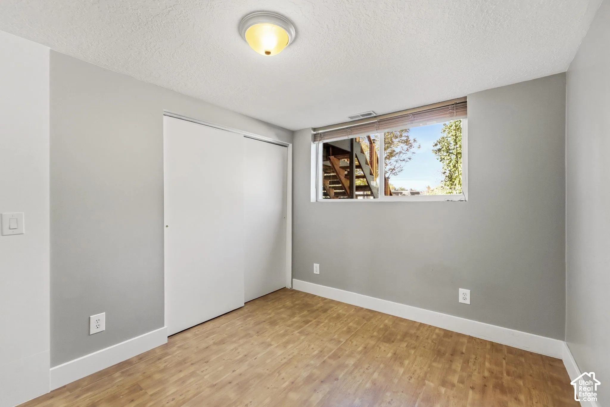 Bright bedroom offering wood-finish flooring, neutral gray walls, and a large window with natural light