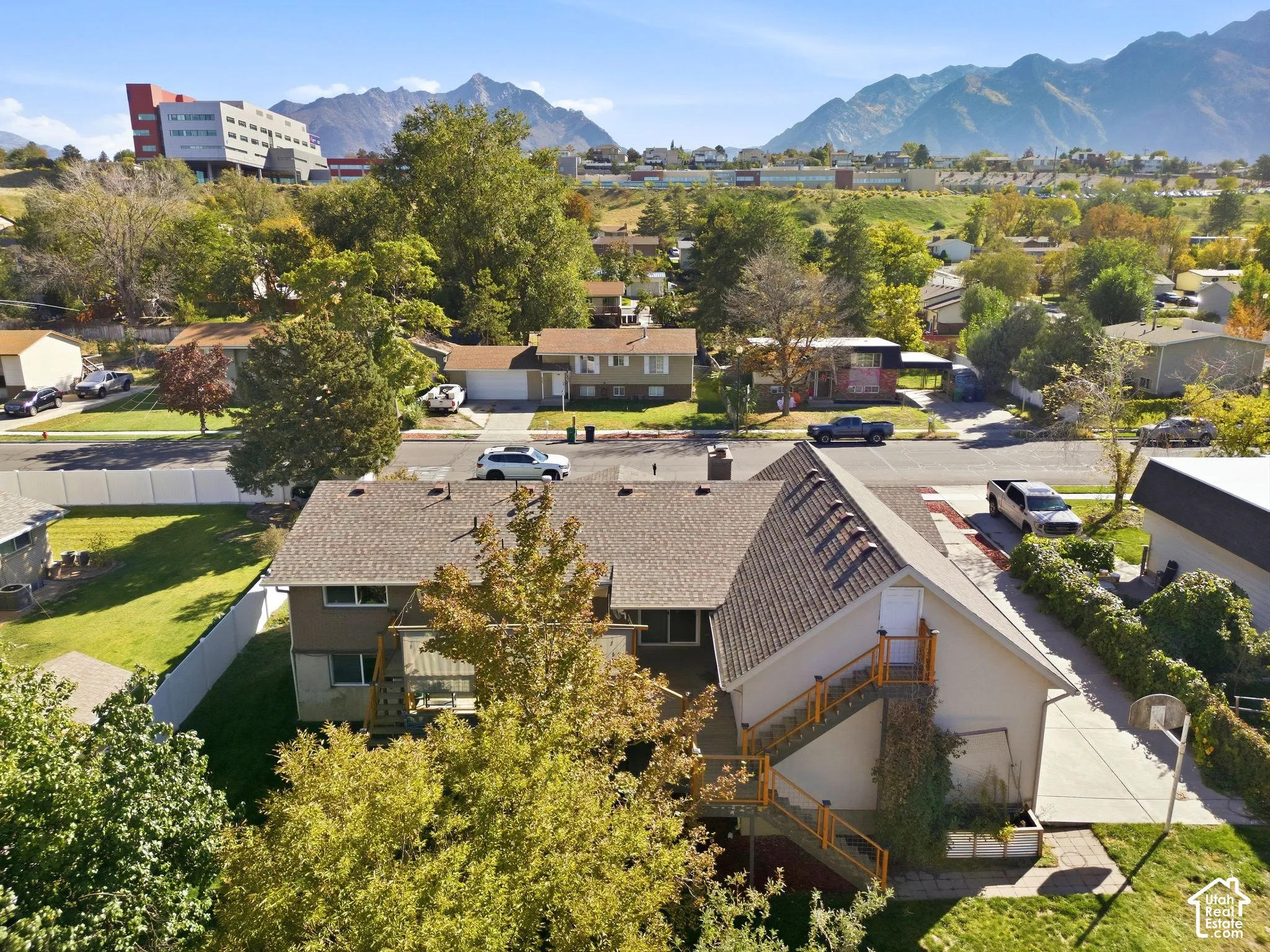 Property featuring a pitched roof, exterior staircase with railing, concrete driveway, and surrounding green spaces