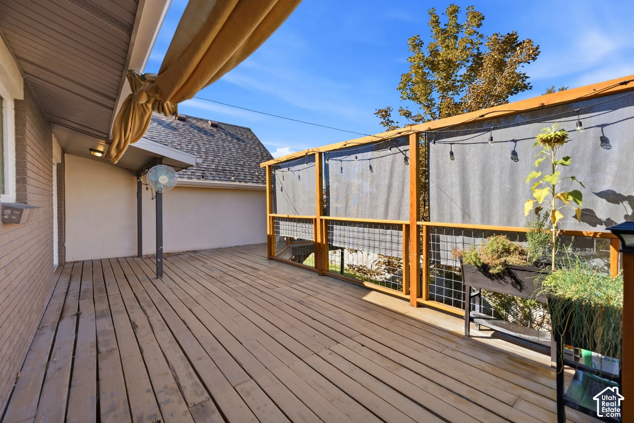 Expansive outdoor deck featuring wood flooring, a built-in privacy screen with string lighting, and an attached awning