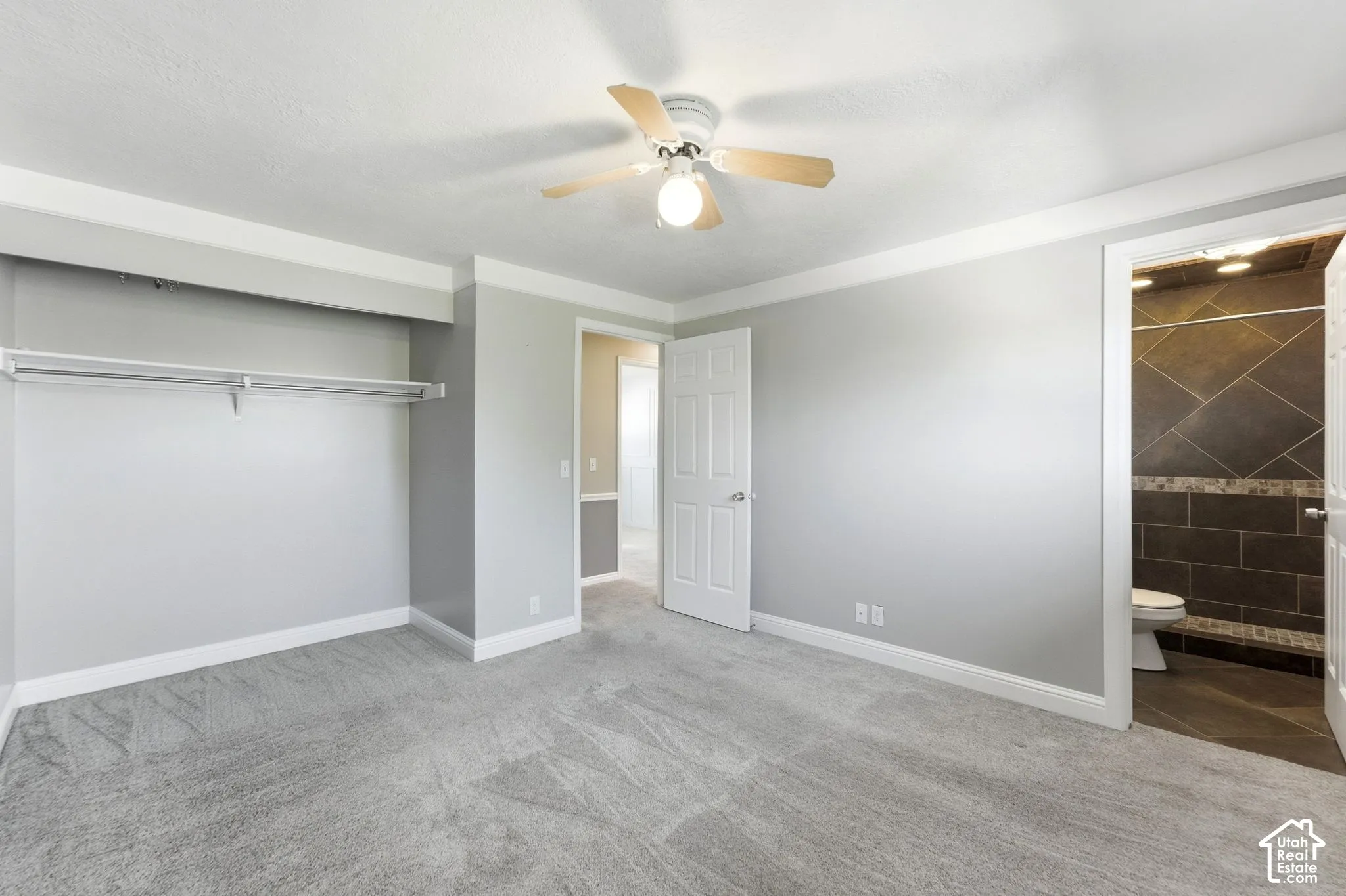 Spacious primary bedroom featuring gray wood-finish flooring, a ceiling fan with integrated lighting, and a large walk-in closet with rod and shelving