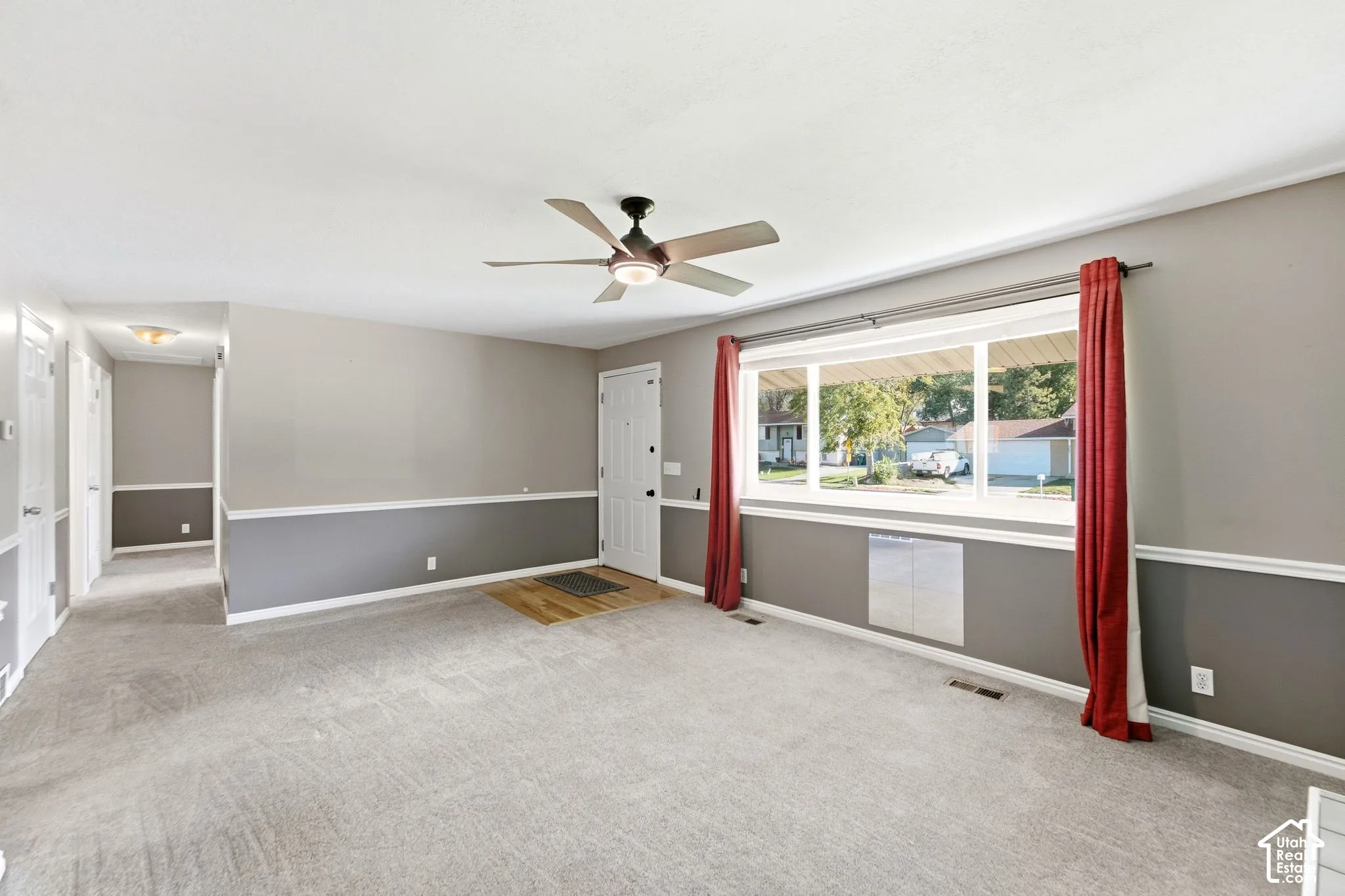Carpeted living space with a ceiling fan, a large picture window, and a white paneled entry door