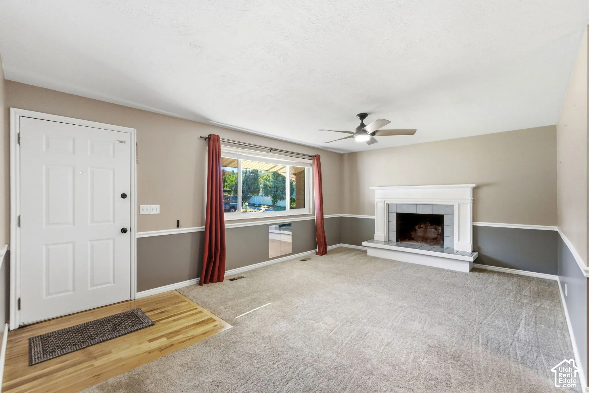 Living area featuring a traditional fireplace with mantel, ceiling fan, and large window