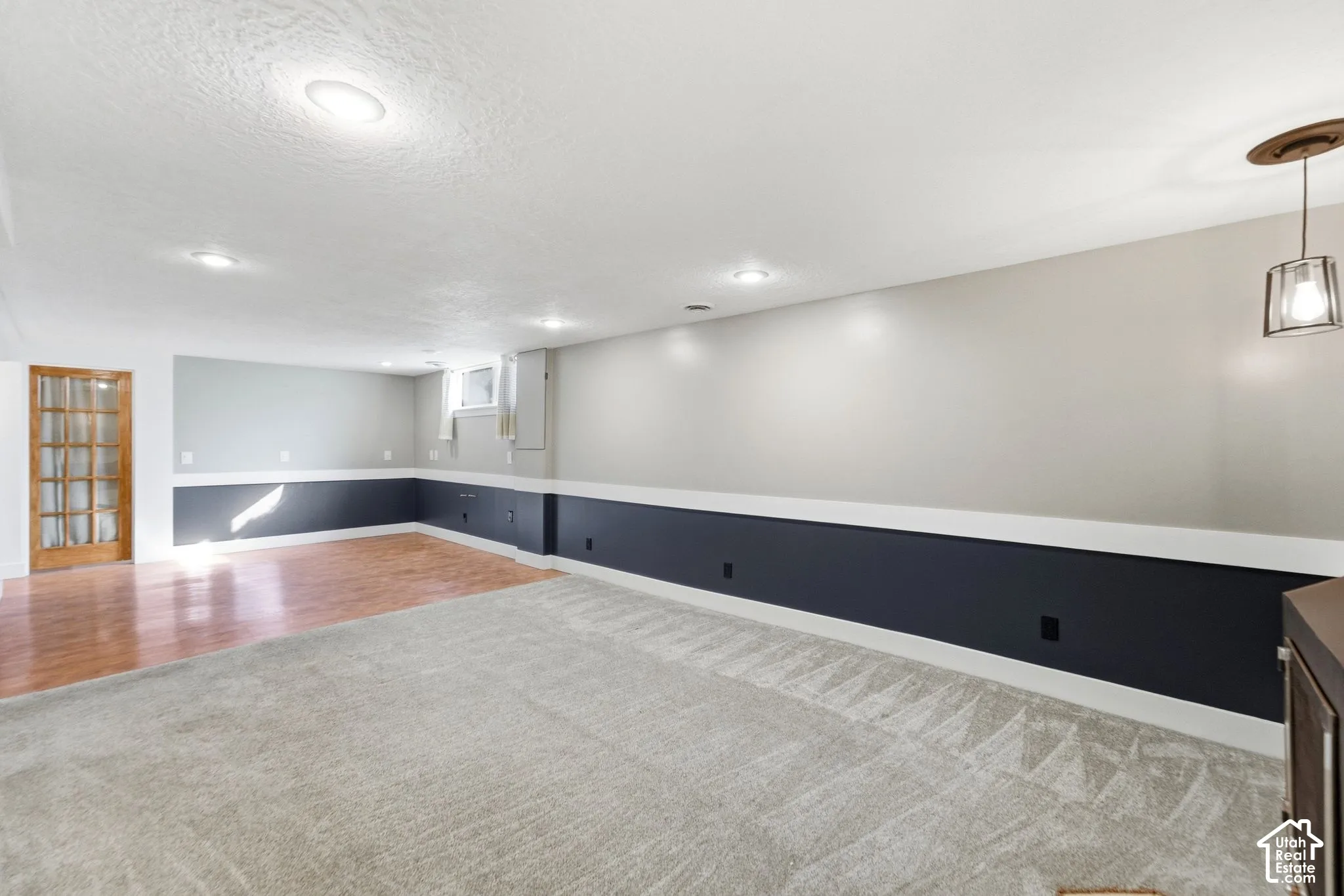 Recessed lighting, wood-finish flooring, light grey carpeting, white ceiling, and a glass-paneled door