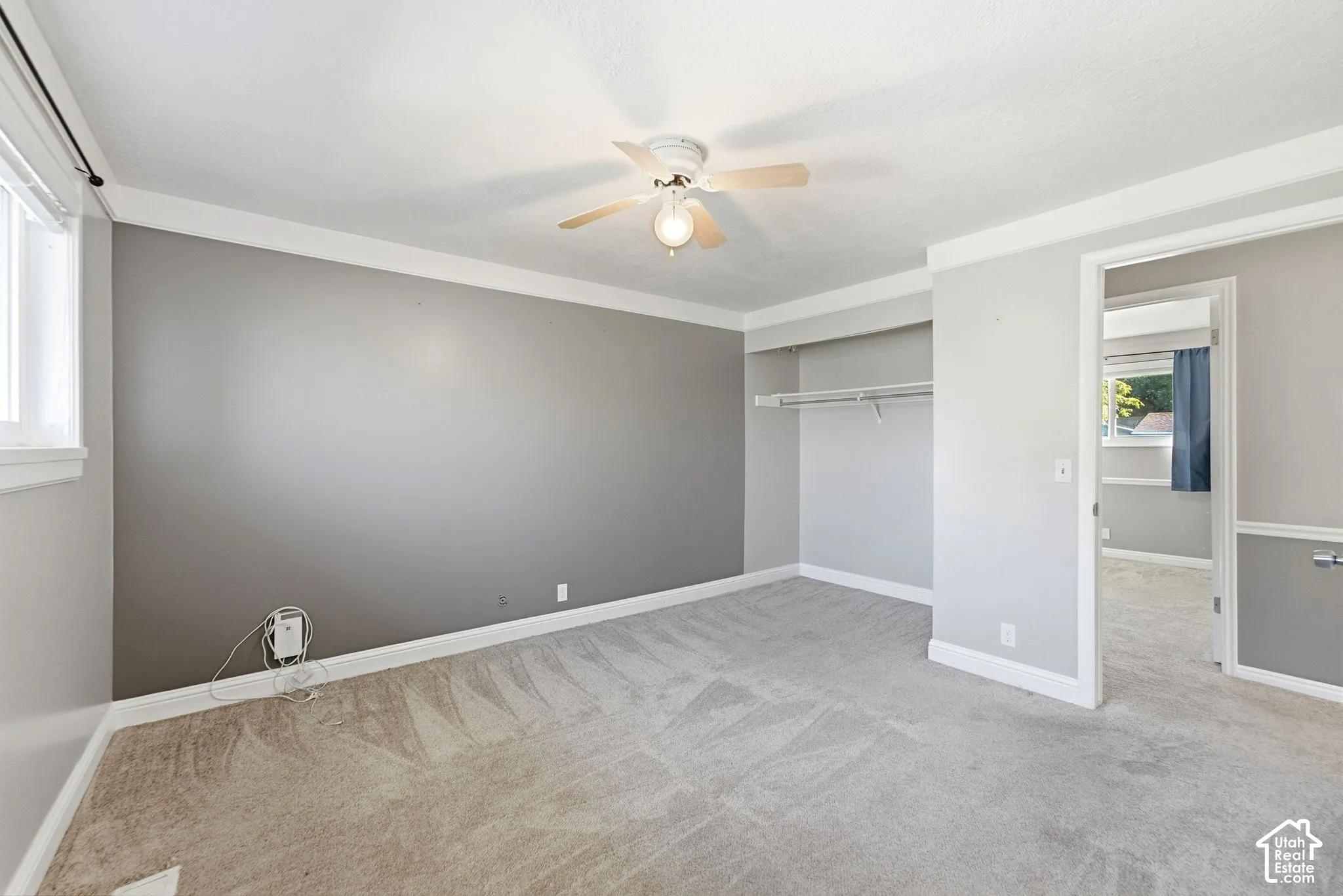 Recessed closet with built-in shelving, ceiling fan with integrated lighting, window with white trim, and light-toned carpeting