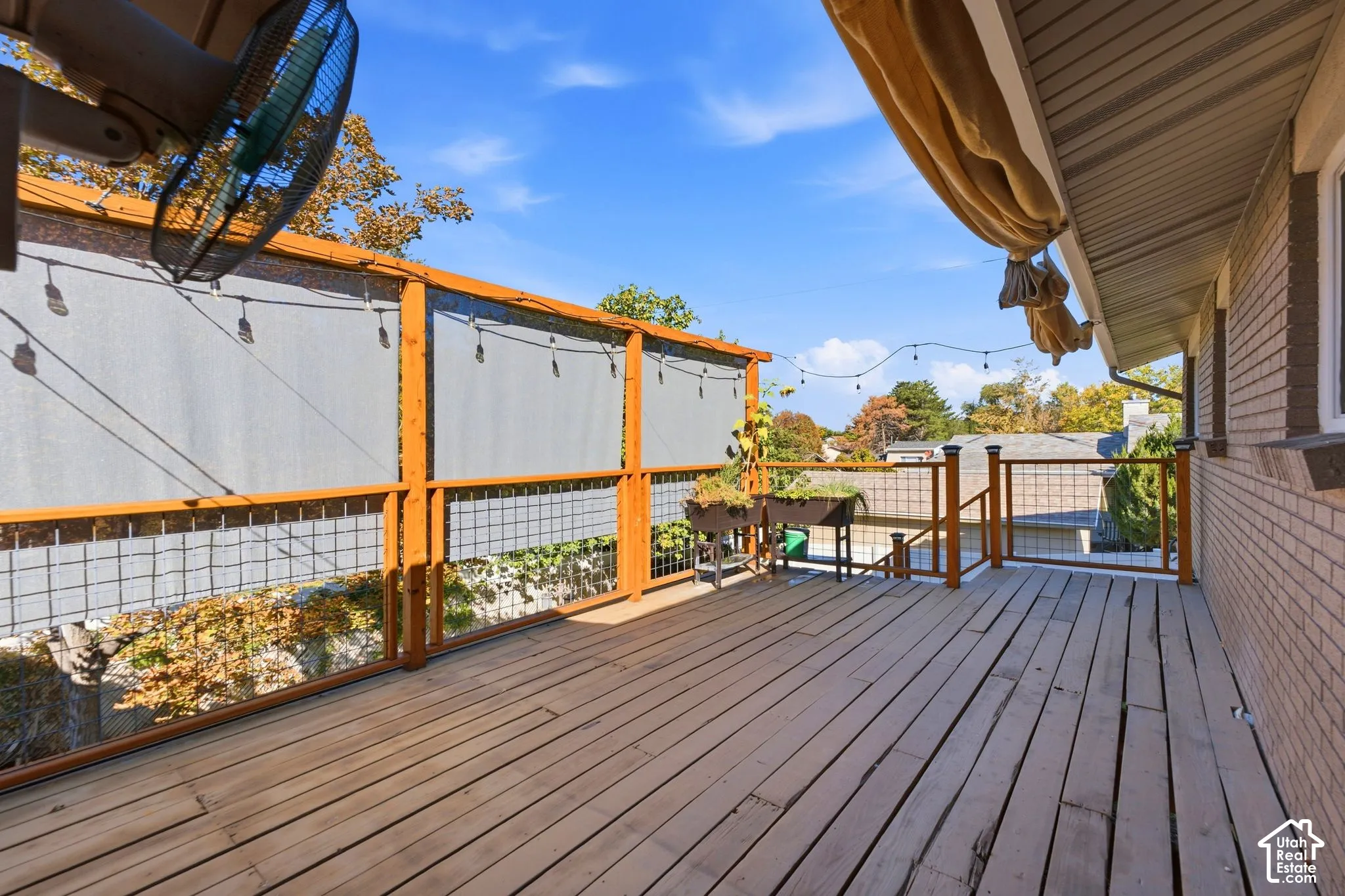 Wood-finish deck with a wood and wire railing system, string lighting, and retractable shades