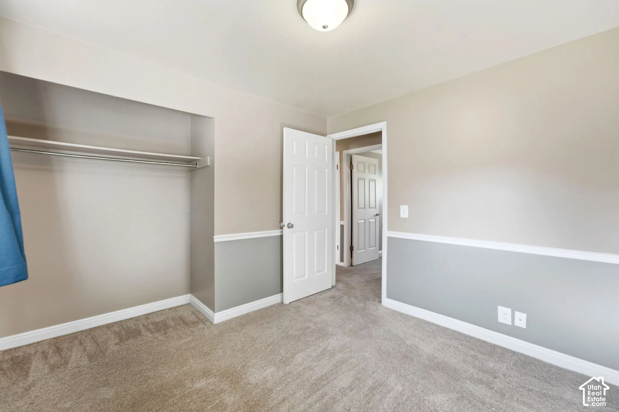 Recessed closet with a metal hanging rod, neutral-toned carpet, two-tone wall paint, white trim, and a flush mount light fixture