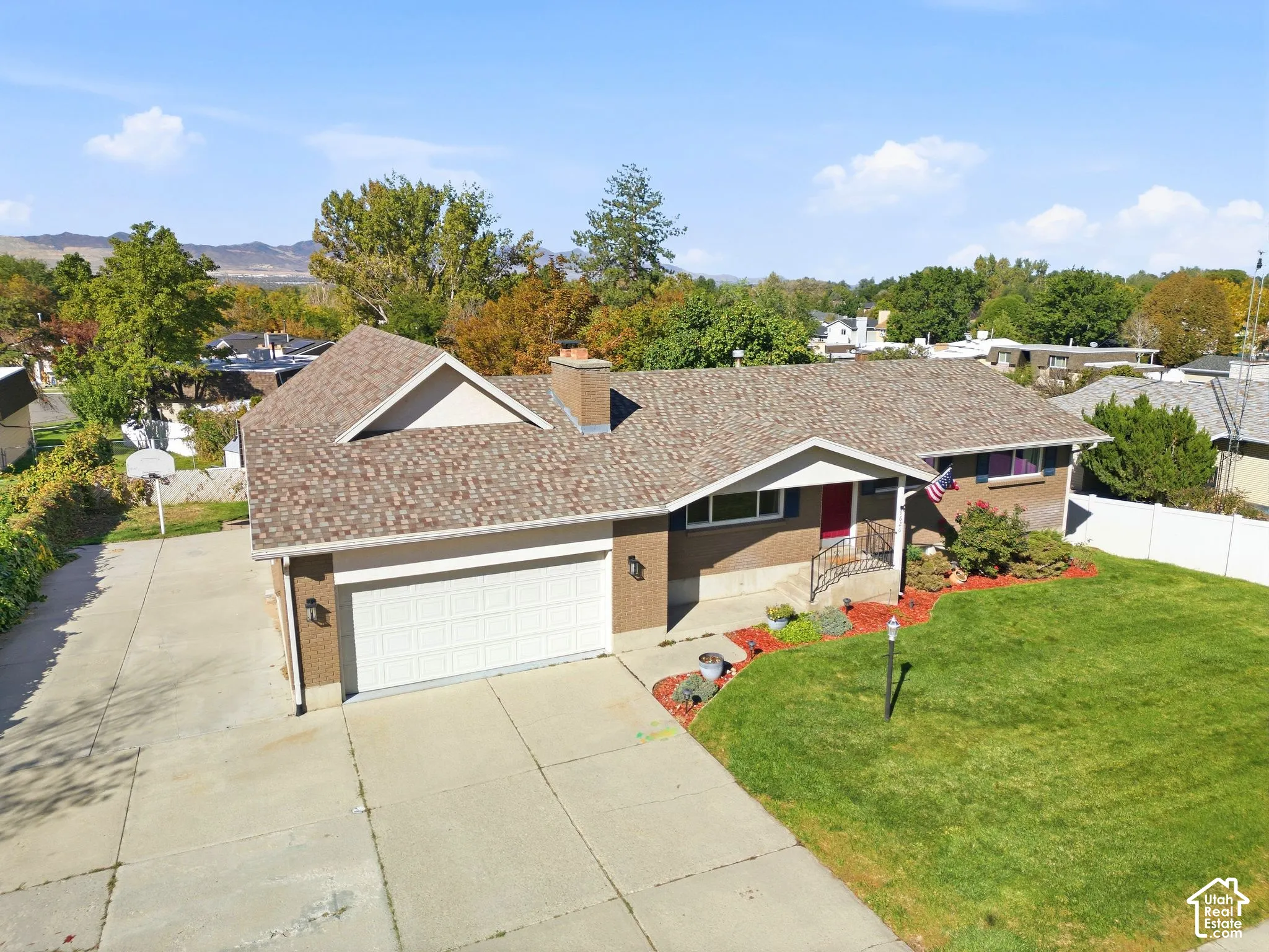 Brick exterior with a shingled roof, extended driveway, attached garage, and manicured front lawn
