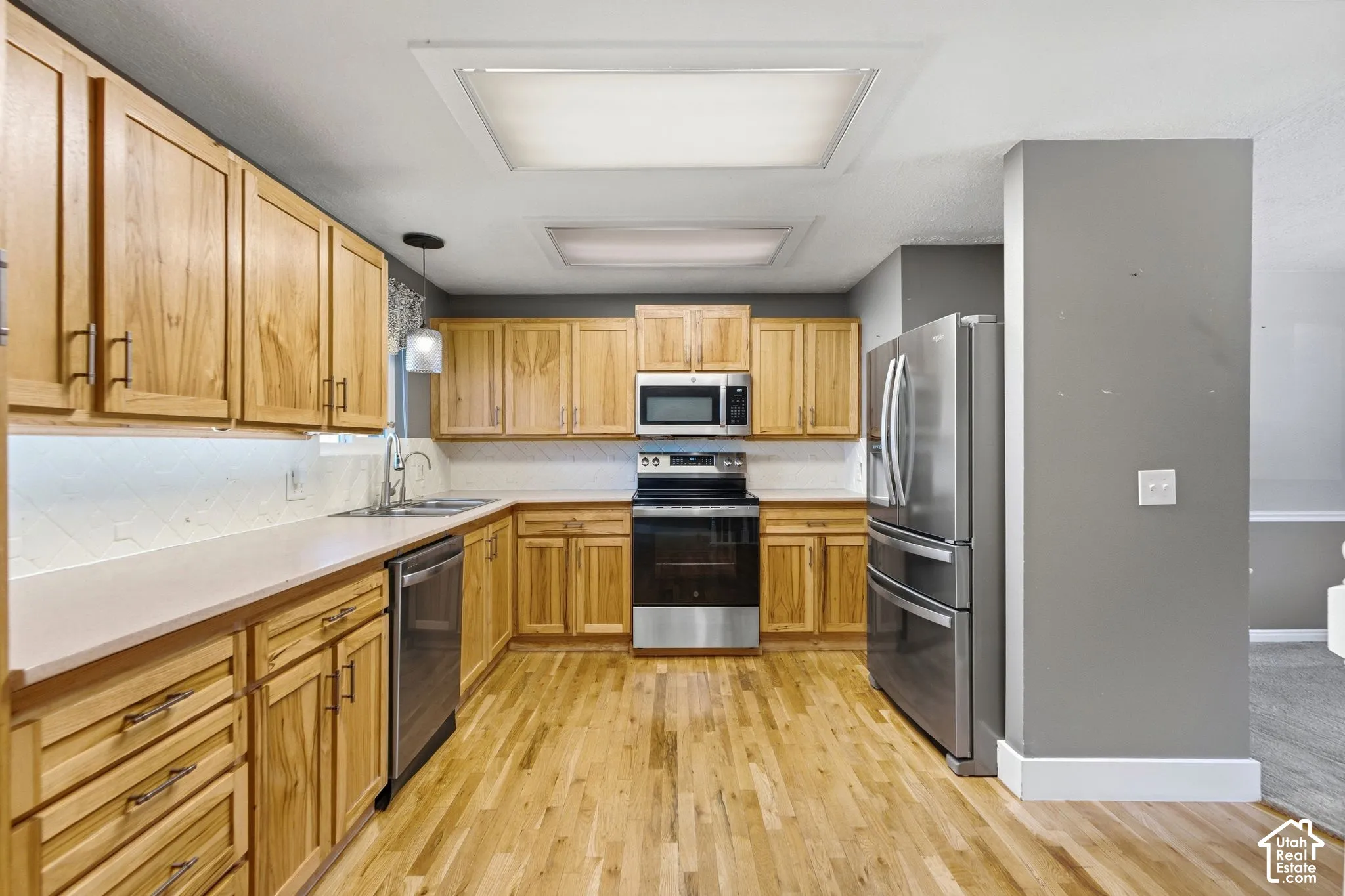 Wood-finish flooring, light wood cabinetry, stainless steel appliances, solid surface countertops, and recessed ceiling lighting