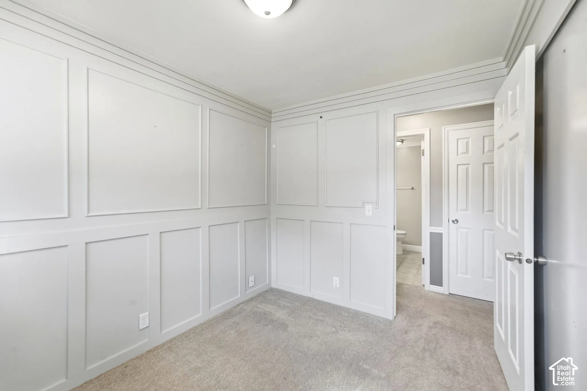 Neutral-toned carpeting, decorative wainscoting paneling, crown molding, and a flush-mount ceiling light fixture