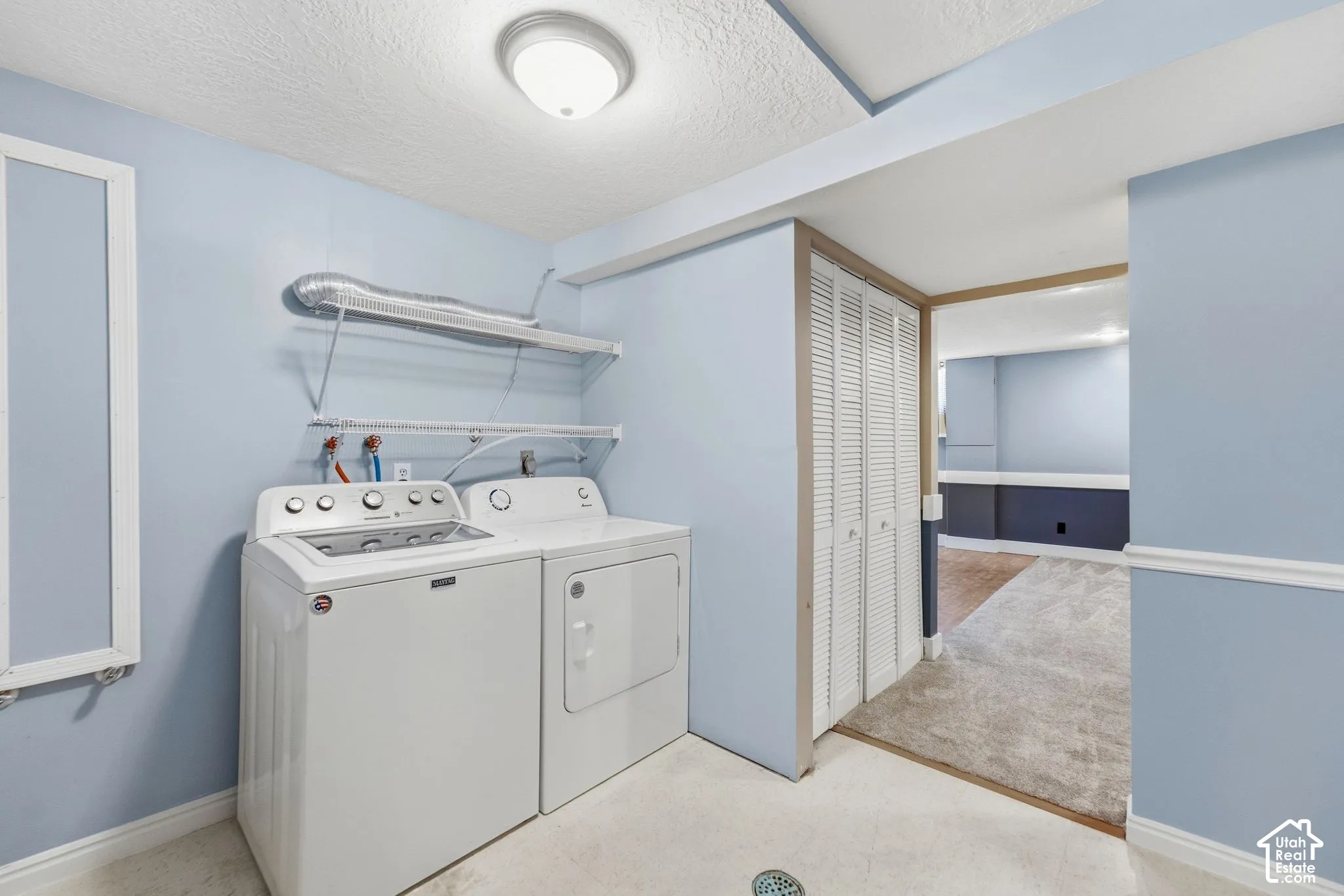 Laundry area featuring light blue walls, overhead lighting, wire shelving, and bi-fold closet doors