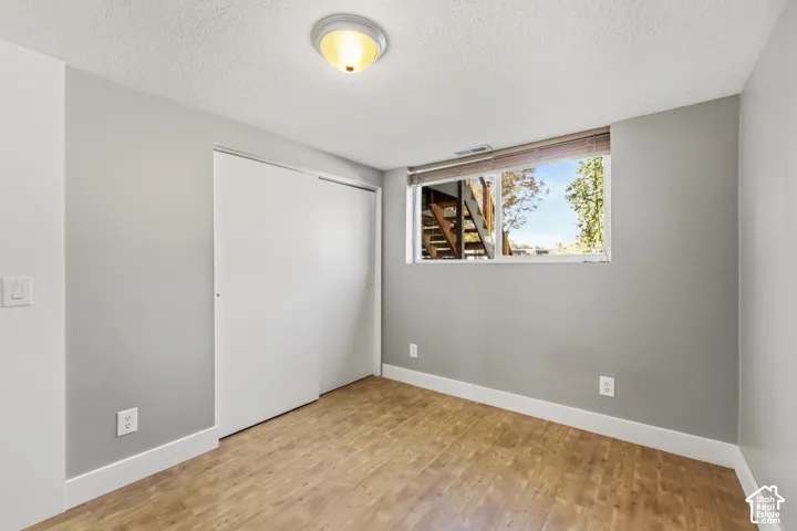 Bright bedroom offering wood-finish flooring, neutral gray walls, and a large window with natural light