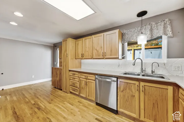 Kitchen featuring wood-finish cabinetry, stainless steel dishwasher, double basin sink, white countertops, and wood-finish flooring
