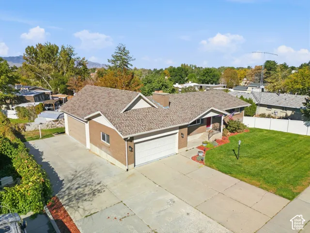 Brick exterior with a peaked roofline, attached multi-car garage, concrete driveway, and a landscaped front yard