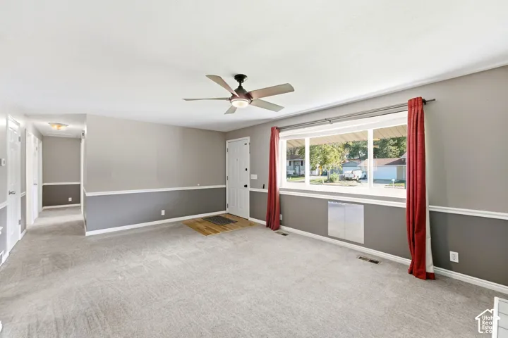 Carpeted living space with a ceiling fan, a large picture window, and a white paneled entry door