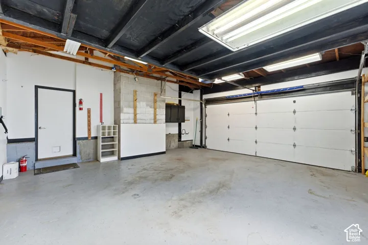 Concrete flooring, exposed ceiling joists, overhead fluorescent lighting, and a white panel garage door