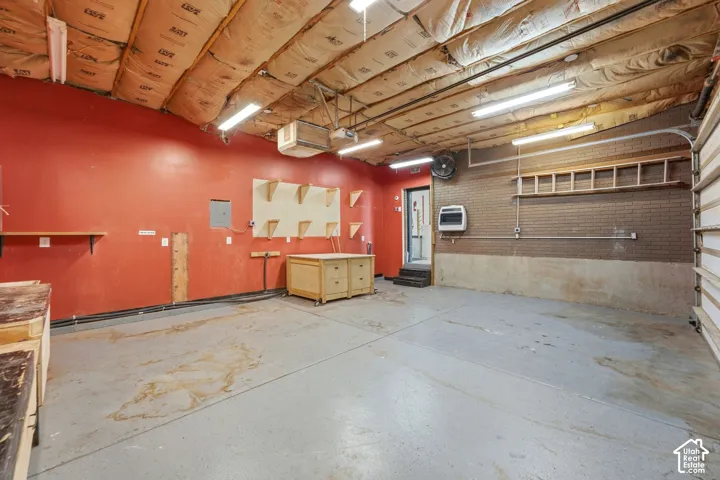 Spacious garage with concrete flooring, exposed ceiling insulation, fluorescent lighting, and a brick accent wall