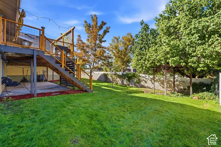 Expansive green lawn, multi-level deck with wood and wire railings, mature trees, and concrete patio under the deck