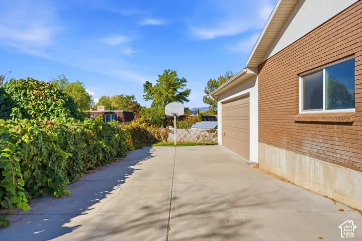 Attached two-car garage with tan doors, brick exterior, concrete driveway, and established perimeter landscaping