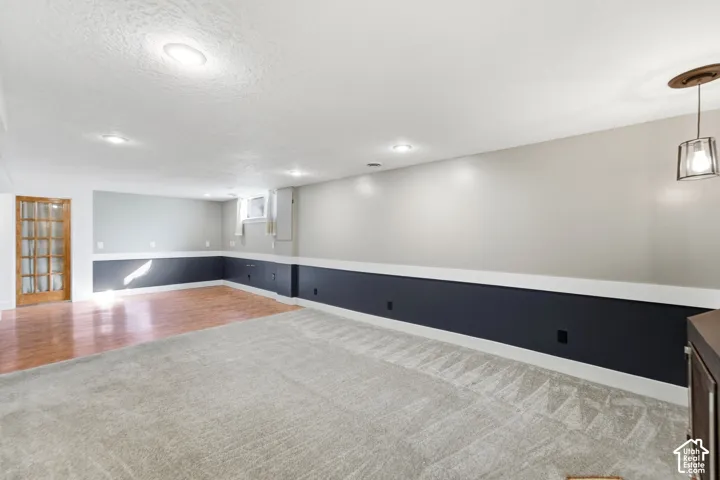 Recessed lighting, wood-finish flooring, light grey carpeting, white ceiling, and a glass-paneled door