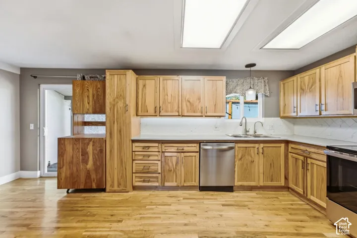 Wood-finish flooring throughout, wood-finish cabinetry, stainless steel dishwasher, white subway tile backsplash, and light-toned countertops
