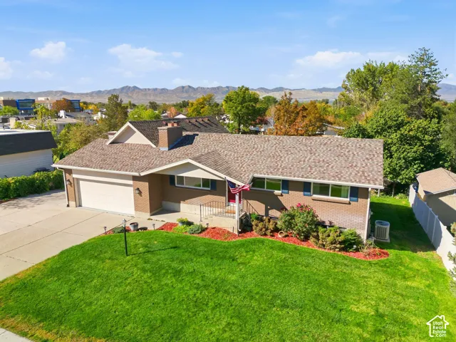 Brick exterior with attached garage, shingle roof, and a mature landscaped front yard