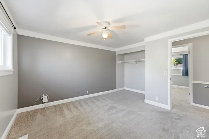 Recessed closet with built-in shelving, ceiling fan with integrated lighting, window with white trim, and light-toned carpeting