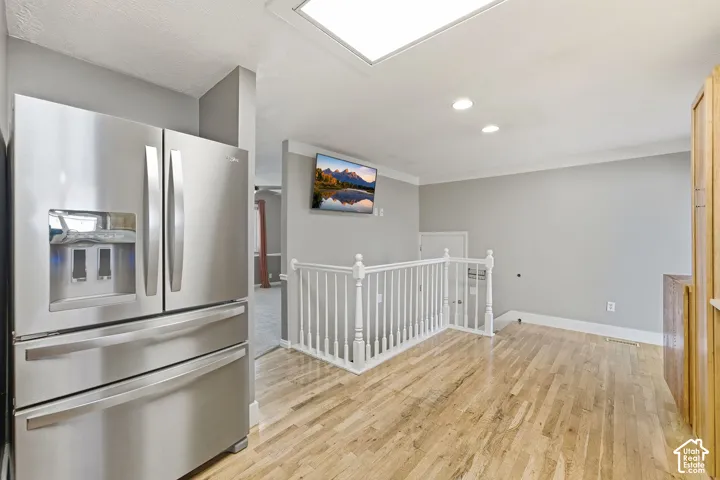 Stainless steel French door refrigerator, wood-finish flooring, white painted railing, recessed lighting, and a skylight