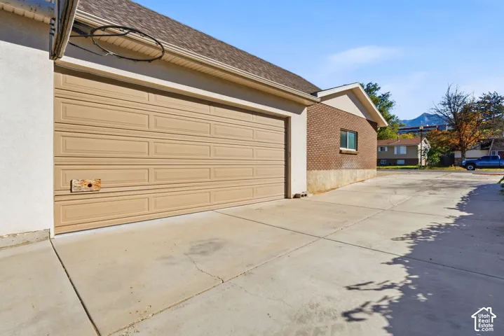 Attached garage with a tan panel door, concrete driveway, and brick exterior accents
