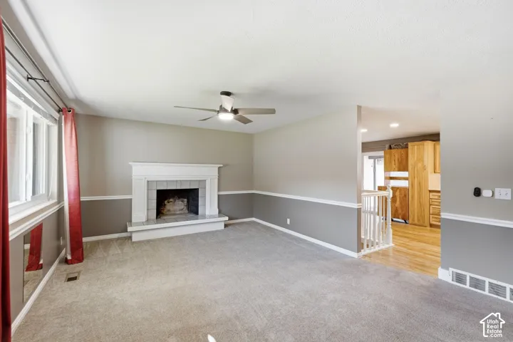 Carpeted living area with a white mantel fireplace, ceiling fan, and large windows