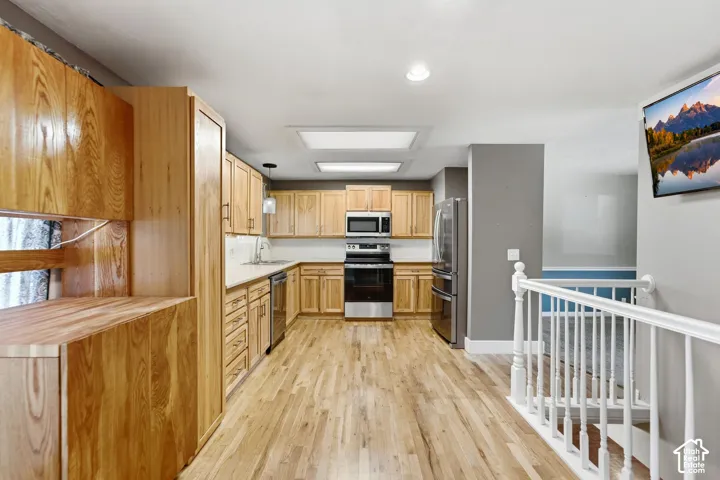 Kitchen featuring wood-finish flooring, light wood cabinetry, stainless steel appliances, and white countertops