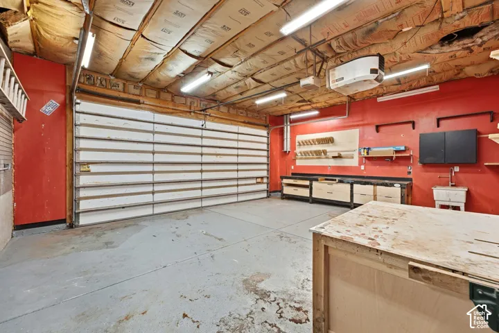 Spacious garage featuring a sectional overhead door, epoxy-coated concrete flooring, exposed wood-beam ceiling with integrated lighting, and built-in wall-mounted cabinetry and shelving throughout