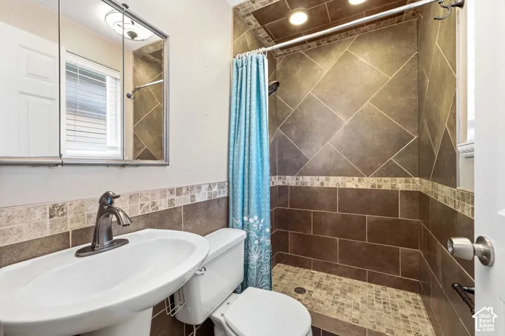 Pedestal sink with a brushed nickel faucet, tiled shower surround, mosaic tile accents, and recessed shower lighting