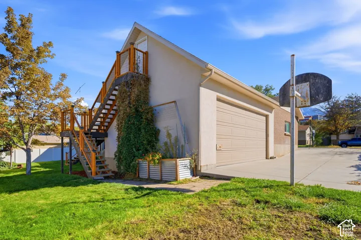 Attached two-car garage with a concrete driveway, exterior staircase with wood railings, and an expansive lawn