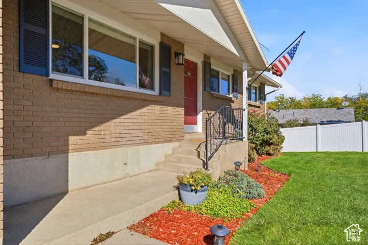 Welcoming front entrance featuring a brick and stone exterior, covered porch with metal railings, and manicured landscaping with ornamental plantings and mulched beds