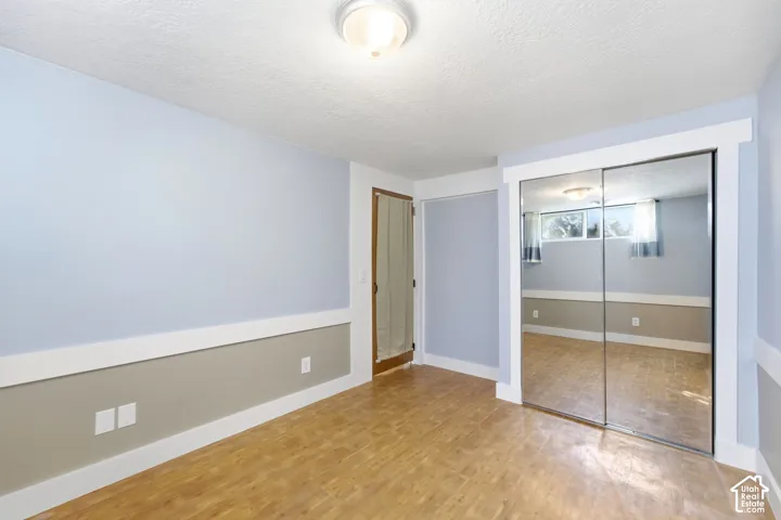Spacious bedroom with wood-finish flooring, mirrored sliding closet doors, two-tone wall treatment with neutral upper and taupe lower sections, and recessed ceiling lighting