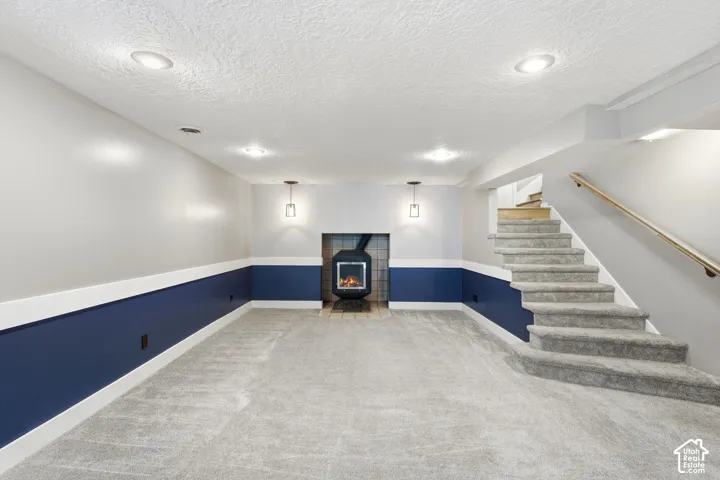 Carpeted flooring, recessed lighting, wall-mounted light fixtures, built-in fireplace, and a staircase with a wood handrail